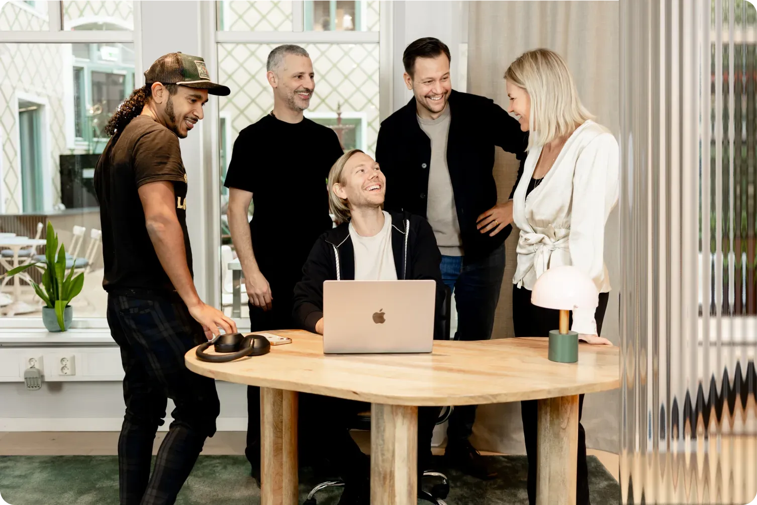 Five colleagues gathered around a desk in the Stockholm office, laughing at something on a laptop
